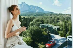 atractivo joven mujer admira el ver de el montañas en el abierto balcón de el hotel posando foto