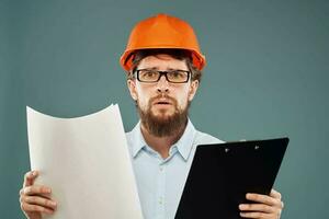 un masculino ingeniero en un naranja difícil sombrero con documentos en el manos de construcción dibujos foto