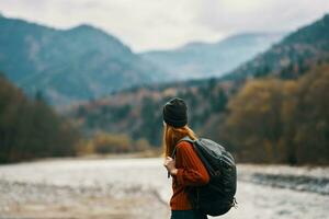 woman in a hat with a backpack are resting in the mountains in nature near the river photo