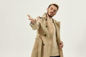 handsome man in beige coat gesturing with hand emotions studio fashion light background photo