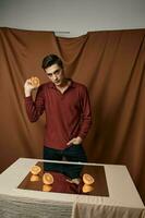 A guy in a shirt and trousers with cut oranges on the table photo