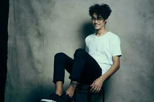 curly-haired guy sitting on a chair with glasses fashion studio photo