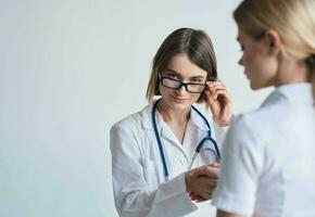 mujer médico en un médico vestido y lentes con un estetoscopio alrededor su cuello y un hembra paciente foto