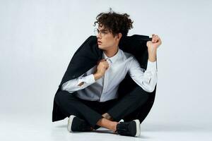 curly-haired guy straightens his jacket over his shoulders and sits on the floor in sneakers and in a suit photo