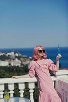 Delighted young girl enjoying a colorful cocktail on the panoramic view hotel terrace Happy female relaxing photo