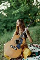 A girl in eco-clothing hippie sitting with a guitar and looking at a sunset in the summer photo