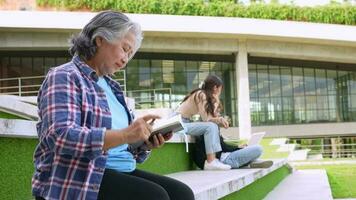 Mature adult student sitting in front off College building and reading school books after attending a university class, Adult education Learning Studying Happy Asian Elderly retired activity video