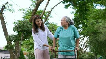 An old elderly Asian woman uses a walker and walking in the garden with her daughter.  Concept of happy retirement With care from a caregiver and Savings and senior health insurance, health care video