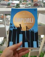 Bekasi, Indonesia in July 2022. A hand is holding a novel titled Rapijali First Edition with the subtitle Mencari by Dee Lestari photo