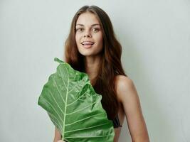 cheerful woman hides behind a green leaf studio light background photo