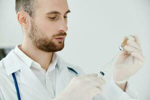 masculino médico participación un jeringuilla en su mano en médico guantes y un estetoscopio ampolla con un vacuna foto