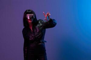 Confused pretty awesome brunet lady in leather jacket trendy specular sunglasses touch invisible object posing isolated in blue violet color light background. Neon party Cyberpunk concept. Copy space photo