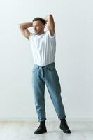 Full body shot of handsome serious tanned man guy in basic t-shirt holds hand behind head posing on white background. Fashion Style New Collection Offer. Copy space for ad. Modeling snapshots photo