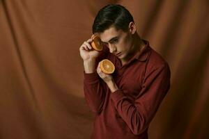 A nice young guy in a red shirt with oranges in his hands holds a close-up near his face. photo