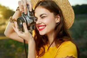 mujer fotógrafo en sombrero mirando dentro el cámara lente sonrisa naturaleza pasatiempo foto