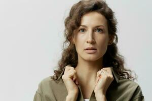 Closeup portrait of serious concentrated curly beautiful woman in casual khaki green shirt holds collar posing isolated on over white background. People Emotions Lifestyle concept. Copy space photo