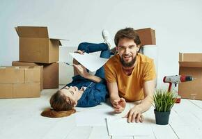 a man and a woman lie on the floor among boxes and a flower in a pot moving photo