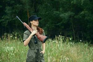 Woman on nature gun on shoulder green jumpsuit travel fresh air green leaves photo