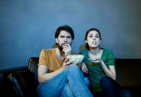 Emotional woman and man on the couch with popcorn watching TV photo