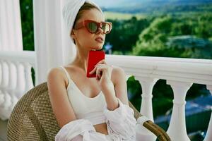 beautiful woman with a red mobile phone sitting on the balcony Perfect sunny morning photo