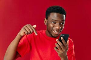 young man of african appearance with mobile phone shows thumb down on red background photo