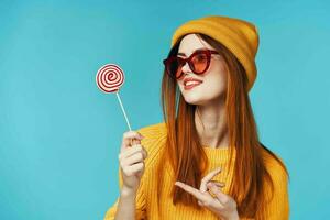 alegre atractivo mujer con lentes pirulí en mano amarillo sombrero azul antecedentes foto