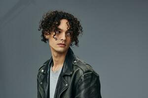 Pensive handsome stylish tanned curly man leather jacket looks aside posing isolated on over gray studio background. Cool fashion offer. Huge Seasonal Sale New Collection concept. Copy space for ad photo