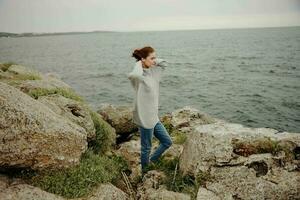 beautiful woman in a gray sweater stands on a rocky shore nature female relaxing photo
