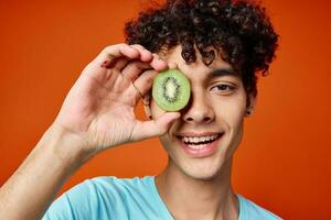 Cheerful guy with curly hair kiwi near the eyes fruit close-up photo