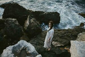 A woman in a white dress stands on the stones by the ocean top view photo