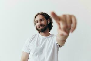 happy man listening to music and smiling in a white t-shirt on a white background and pointing a finger at the screen at the camera photo