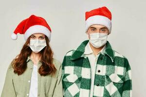 A man and a woman in New Year's Santa hats are standing side by side in medical masks. Close-up protection. Studio photo