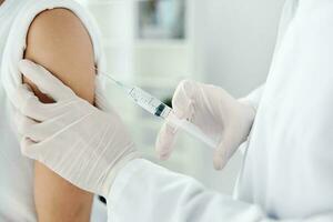 médico en protector guantes sostiene un mujer mano y un inyección de covid-19 vacuna foto