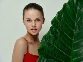 woman stands behind palm leaf on light background red swimsuit clean skin photo
