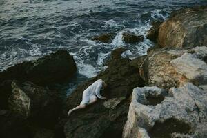 Beautiful bride in long white dress wet hair lying on a rocky cliff view from above photo