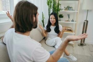 A man and a woman sit on the couch at home in white T-shirts and shouting communicate scandalously do not understand each other. A quarrel in the family of two spouses and aggression, sad emotions photo