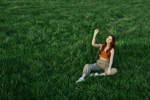 Female student freelancer sits on the grass in the park and watches the sunset, the concept of harmony with the world and nature photo