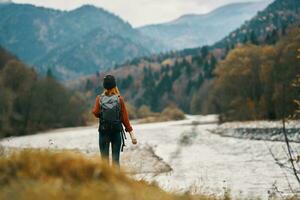 mujer en vacaciones con un mochila en el río banco en el montañas foto
