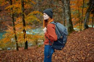 woman with backpack walking in the autumn park near the river in nature side view photo