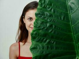 sonriente mujer en un traje de baño echar un vistazo fuera desde detrás un verde hoja estudio foto