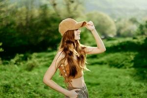 un joven mujer con un atlético cuerpo camina en un verano verde parque en naturaleza. puesta de sol luz de sol ilumina su rojo pelo foto