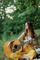 A girl in eco-clothing hippie sitting with a guitar and looking at a sunset in the summer photo