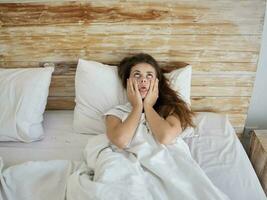 woman lying in bed grimacing showing tongue hands on face photo