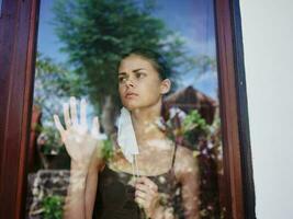 masked woman looking out the window sad look lockdown photo