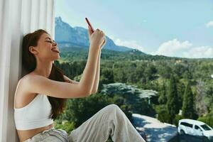 retrato mujer utilizar el teléfono mira a el pantalla en un cómodo hotel un abierto ver de el estilo de vida foto