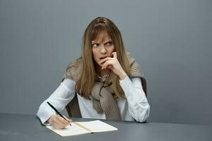 Nervous young blonde student lady freelancer in warm sweater writing letter recline on hand look aside sitting at workplace in gray modern home office. Education Career Profession Concept. Copy space photo