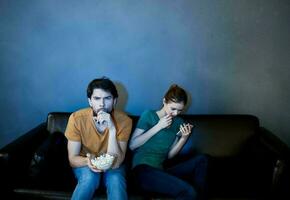 An emotional man and a pretty woman on the couch are watching TV with interest in a dark room photo