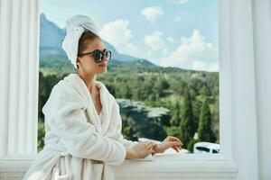 elegante mujer en un bata de baño en el Mañana en el balcón admirativo naturaleza Perfecto soleado Mañana foto