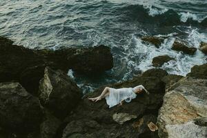beautiful woman in a white dress lying on a stone in a white dress view from above photo