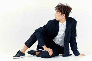 fashionable guy in a suit and sneakers sitting on the floor in a bright room curly hair model photo